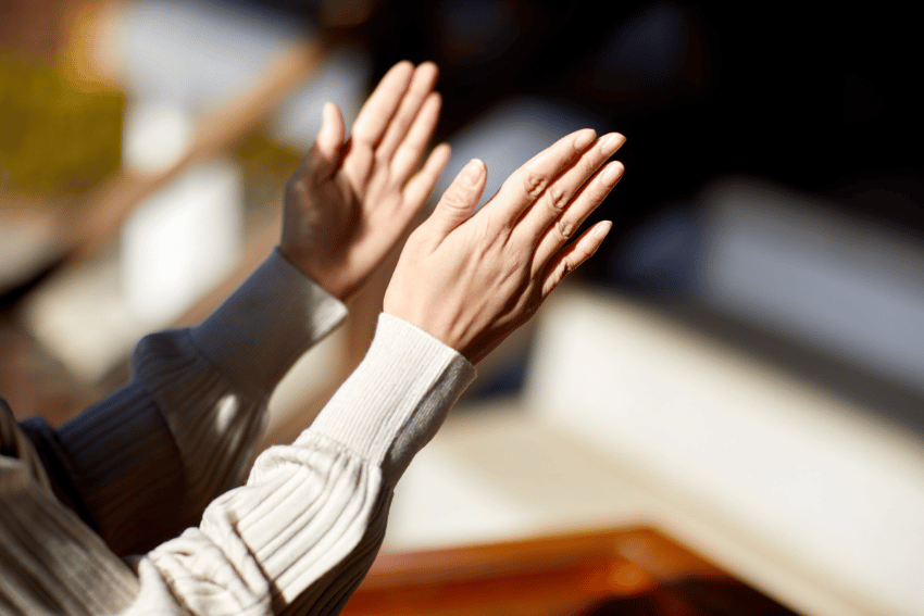 A close-up of a person's hands held open in front of them, palms facing upward, as if demonstrating how to break up a dog fight. The person is wearing a light-colored, long-sleeved sweater. The background is blurred.