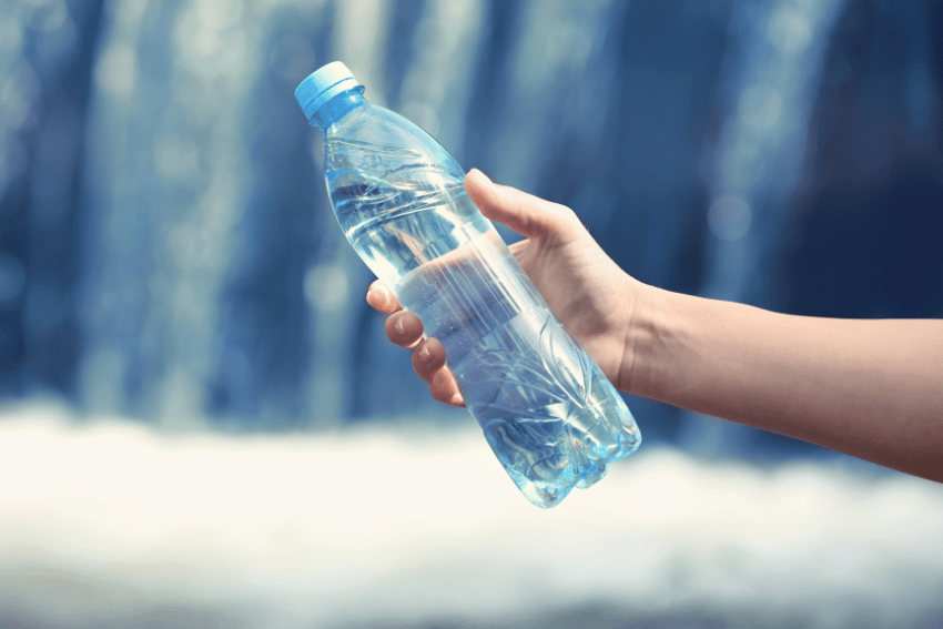 A hand holding a clear plastic water bottle with a blue cap, against a blurred background of flowing water—sometimes, tools like this are recommended in guides on how to break up a dog fight safely and effectively.